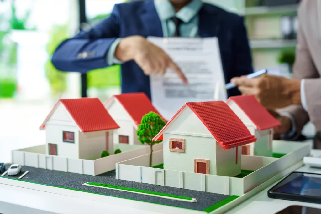 maqueta de casas, con personas seleccionando un papel al fondo.