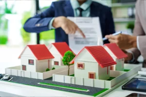 maqueta de casas, con personas seleccionando un papel al fondo.